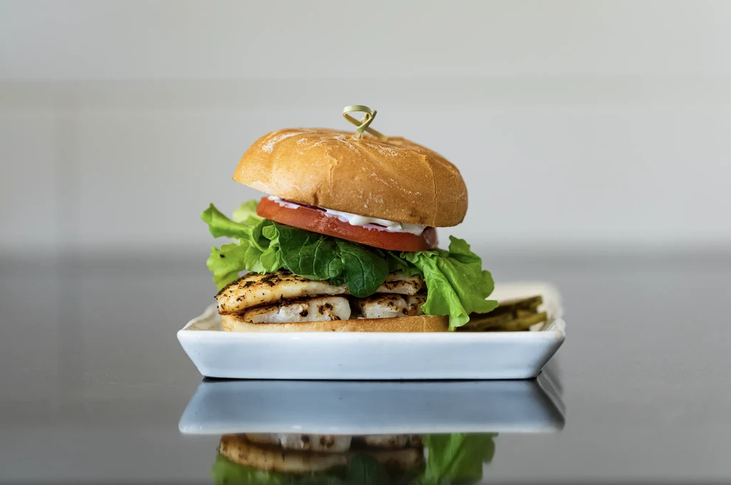 Grilled sandwich with lettuce, tomato, sauce, and pickles on a white plate.