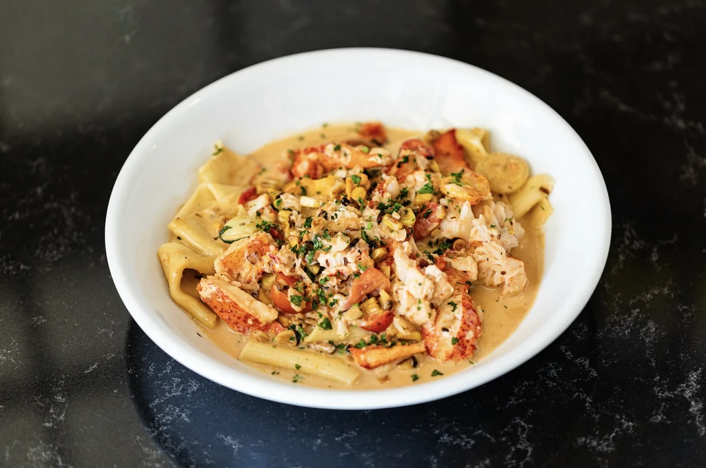Close-up of creamy lobster pasta with sweetcorn, vegetables, and herbs.
