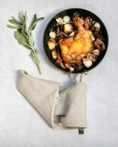 Roasted chicken leg with vegetables and sage in a dark frying pan.