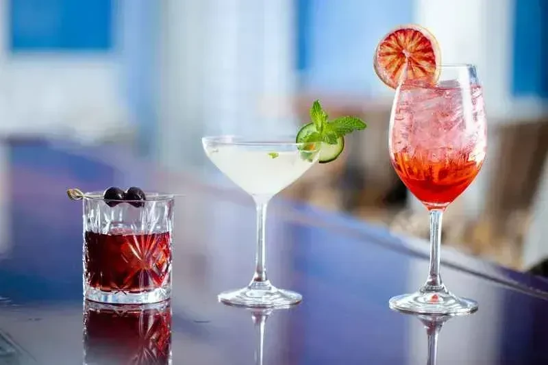 Three distinct cocktails with various garnishes on a reflective counter.