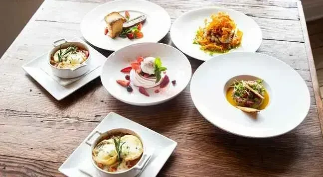 Six artfully plated dishes, including dessert and savory, on a wooden table.