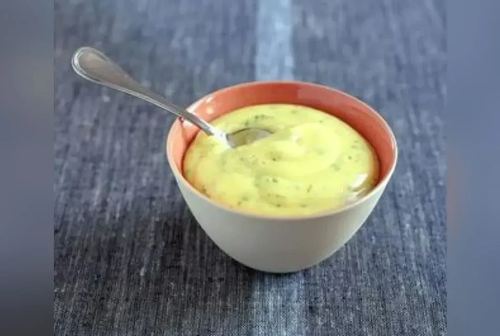 Creamy yellow herb sauce in a ceramic bowl with a spoon.