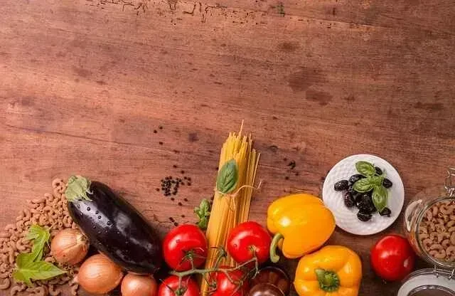 Fresh vegetables, pasta, and olives arranged on a rustic wooden surface.