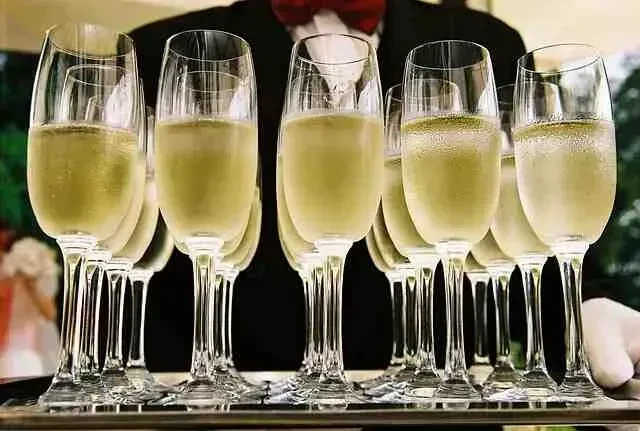 Multiple sparkling flutes on a tray, held by formally dressed server.