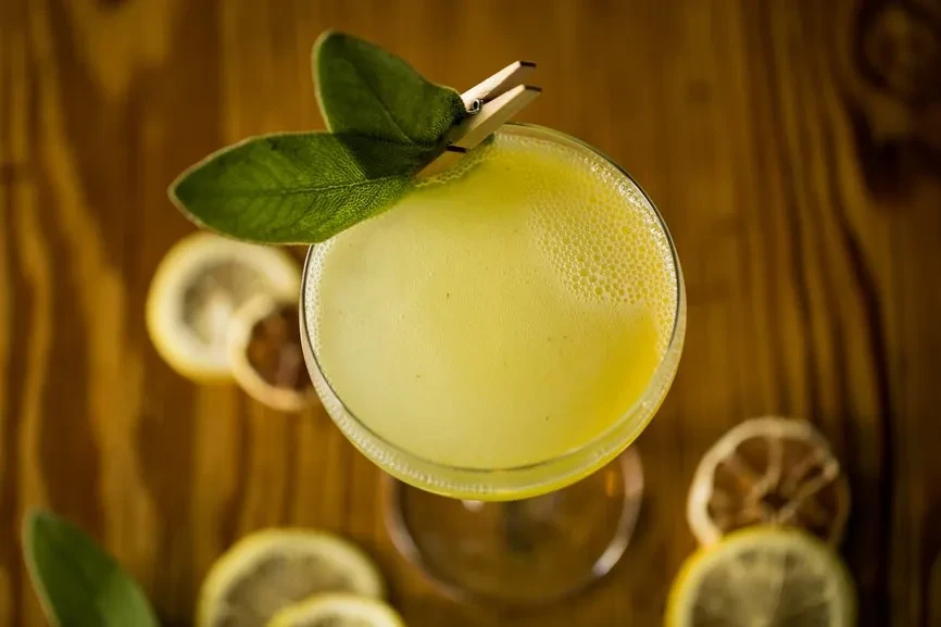 Frothy yellow cocktail with leaf garnish, clothespin, and lemon slices.