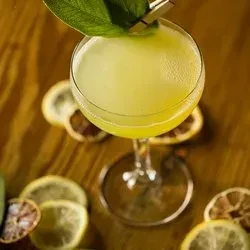 Yellow-green foamy cocktail in coupe glass with leaf and citrus.
