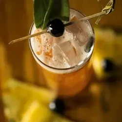 Golden-orange cocktail with ice, foam, green leaf, and skewered cherry.
