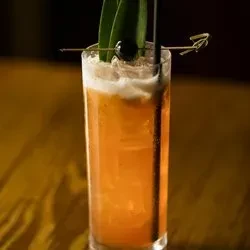 Amber-orange cocktail, frothy, with leaf garnish, cherry, and black straw.
