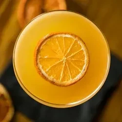 Vibrant yellow-orange cocktail in martini glass with dried orange slice.