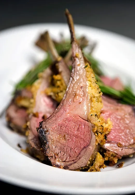 Medium-rare lamb chops with golden crust and green garnish.