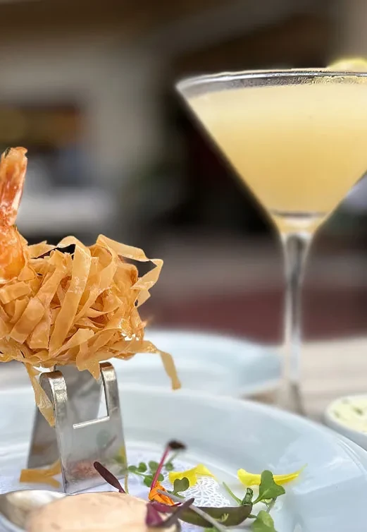 Crispy fried appetizer with microgreens, sauce, and blurred cocktail.