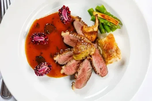 Plated duck breast with crispy skin, asparagus, and pomegranate seeds.