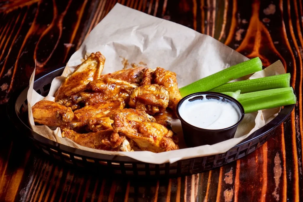 Crispy buffalo wings, celery, and dip in a basket on wood.