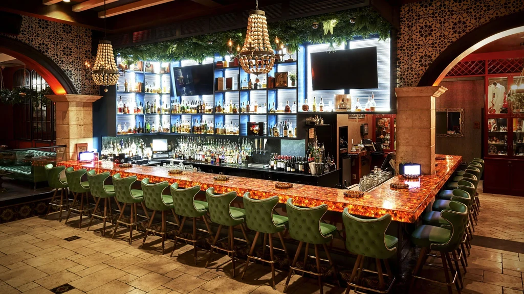 Luxurious bar interior with orange counter, green stools, and blue backlit liquor.