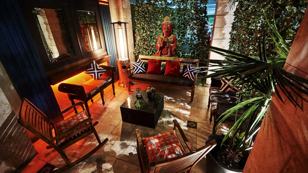 Empty restaurant patio with Buddha statue, patio heater, and warm lighting.