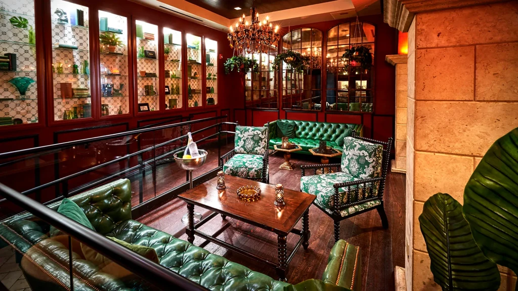 Elegant lounge with green Chesterfield sofas, red walls, and ornate chandelier.