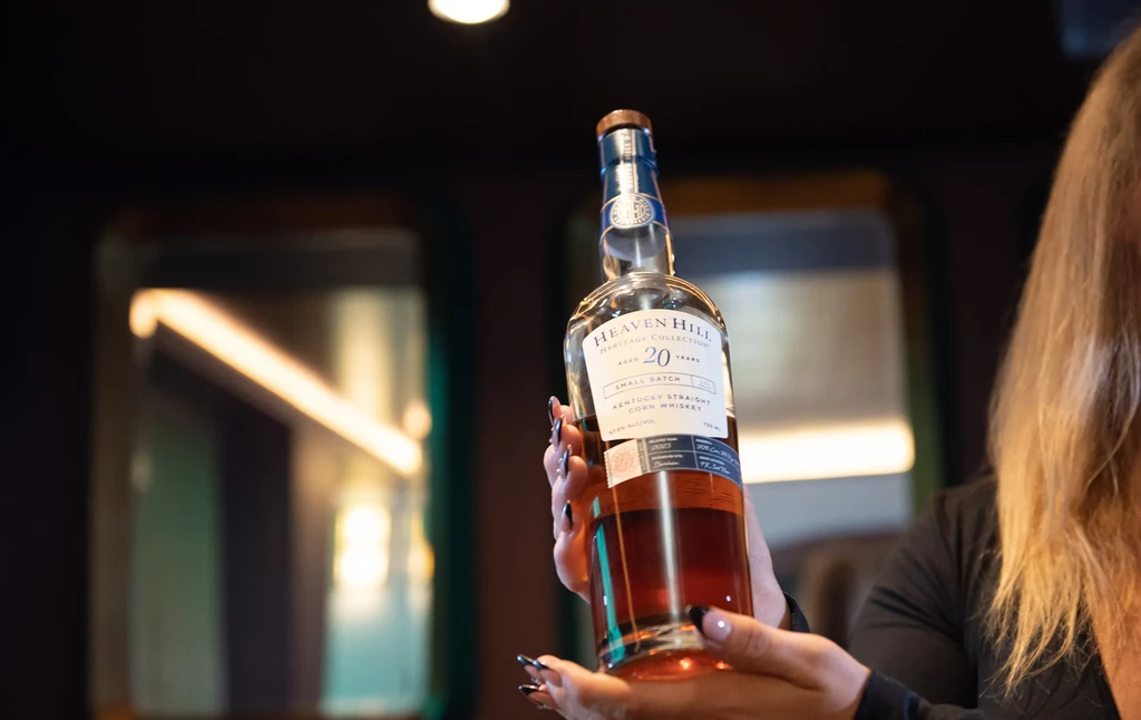 Heaven Hill 20-Year Corn Whiskey bottle held by hands with dark nails.