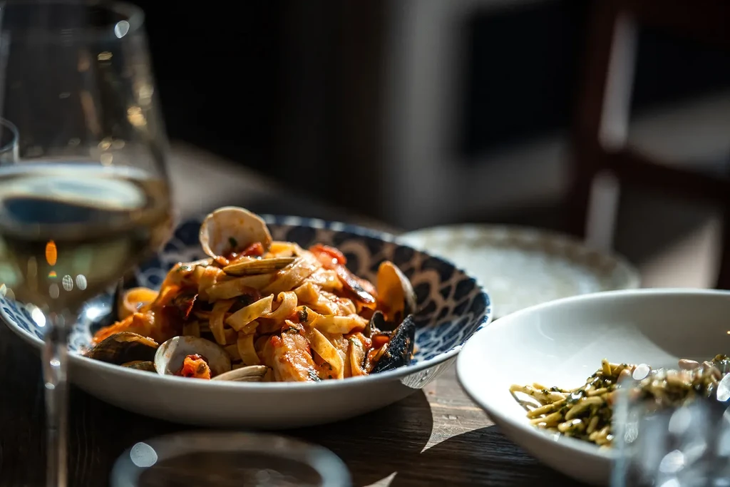Close-up: vibrant seafood pasta with clams in a patterned bowl.
