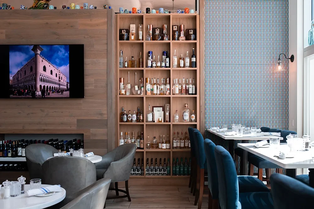 Modern restaurant interior with bottle-filled shelves, a TV, and various seating.
