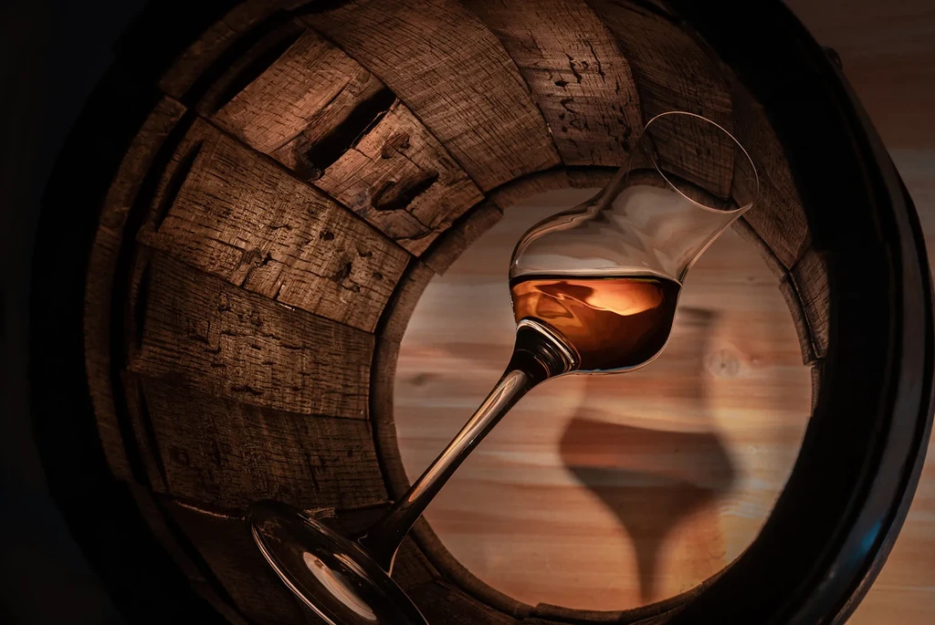 Stemmed glass with amber liquid rests in rustic wooden barrel opening.
