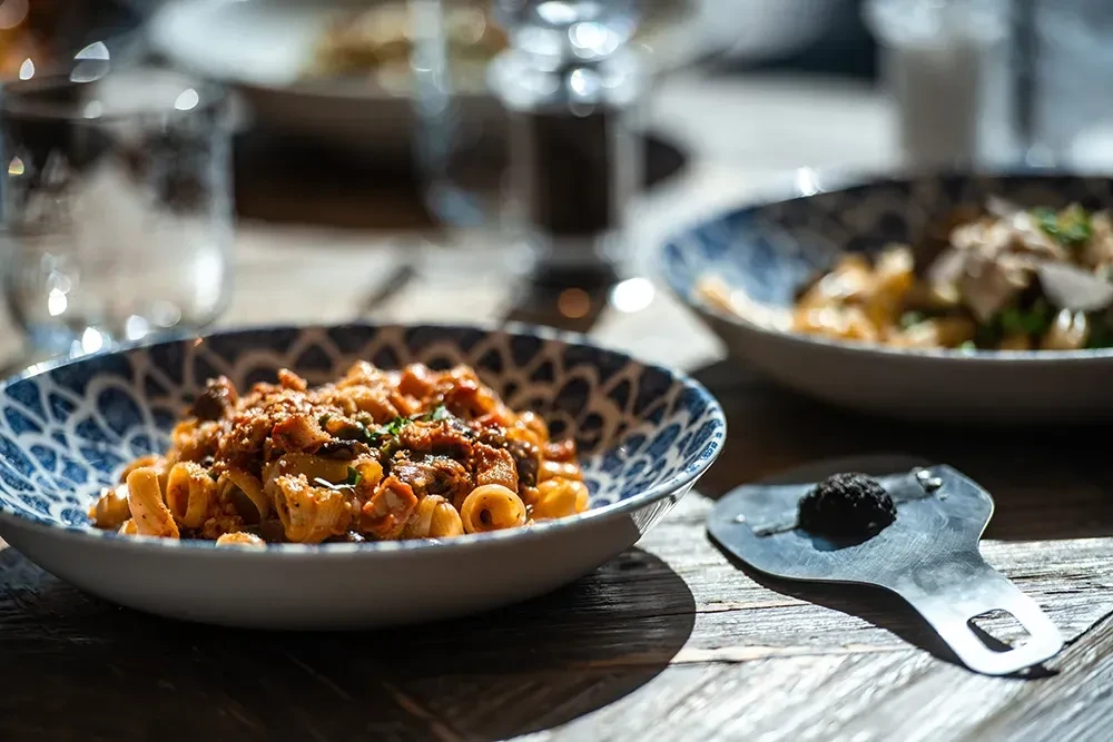 Rigatoni pasta with rich sauce and herbs, beside a truffle and shaver.