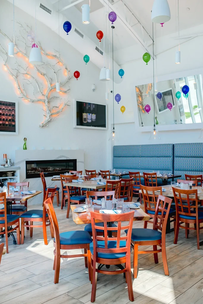Modern restaurant interior with set tables, blue seats, and festive balloons.