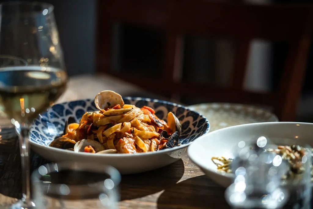 Blue ceramic bowl of fettuccine with clams and red sauce.