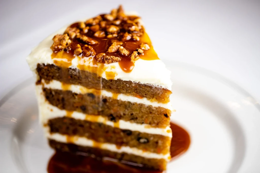 Multi-layered cake slice with cream cheese frosting, caramel, and nuts.