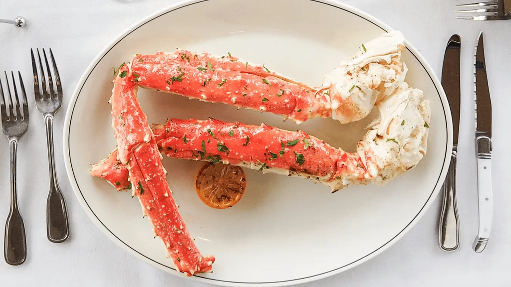 Cooked red-orange crab legs on a plate with lemon, herbs, and cutlery.