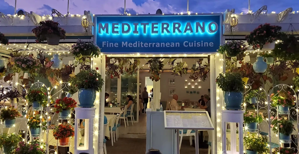 Mediterrano restaurant entrance decorated with plants, fairy lights, and blue neon sign.
