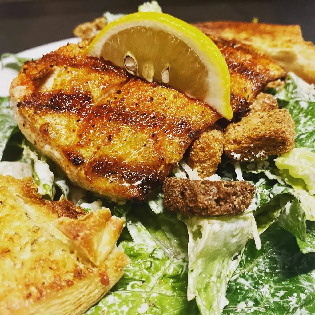 Close-up of chicken Caesar salad with lemon, croutons, and toasted bread.