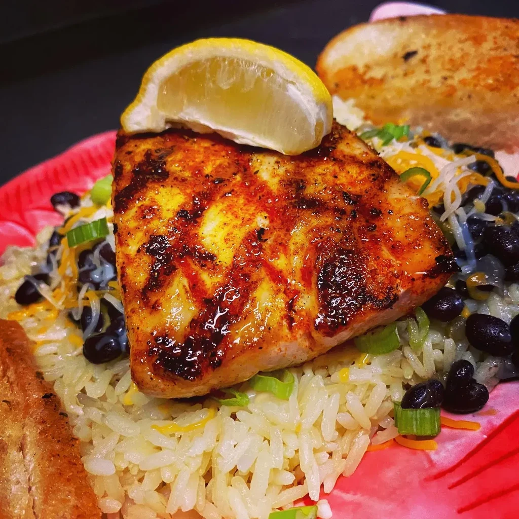 Grilled fish with lemon, rice, beans, cheese, and onions.