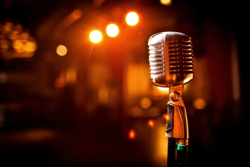 Vintage silver microphone in focus with warm, blurred stage lights.