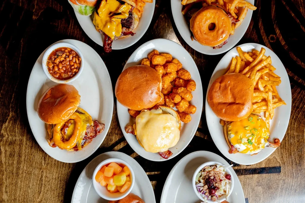 Overhead shot of multiple burgers and side dishes on a wooden table.