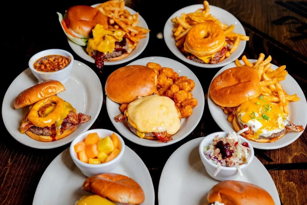 Flat lay of multiple burgers and various sides on a dark table.