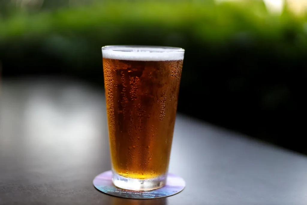 Condensation-beaded glass of amber beer with a frothy head outdoors.