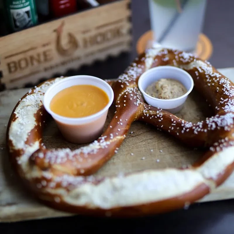 Salted soft pretzel with cheese sauce and mustard on a wooden board.