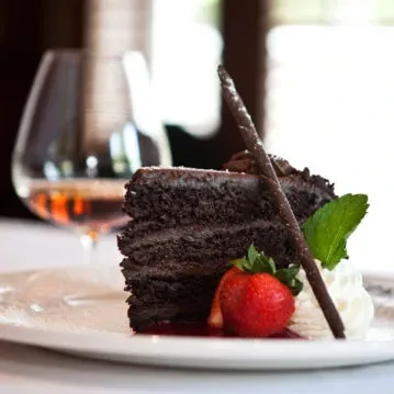Dark chocolate layer cake slice with strawberry, mint, cream, and chocolate sticks.