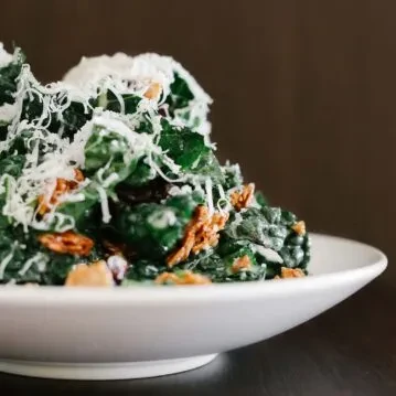 White bowl of creamy greens with grated cheese and crispy bits.