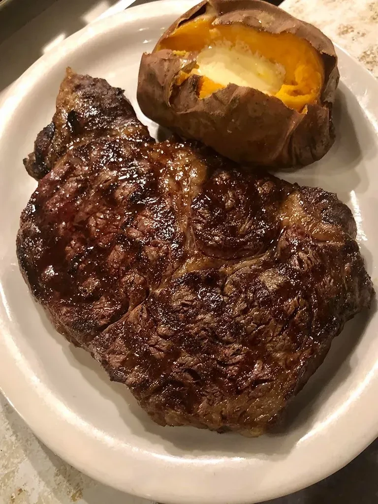 Seared steak, baked sweet potato with butter on a white plate.
