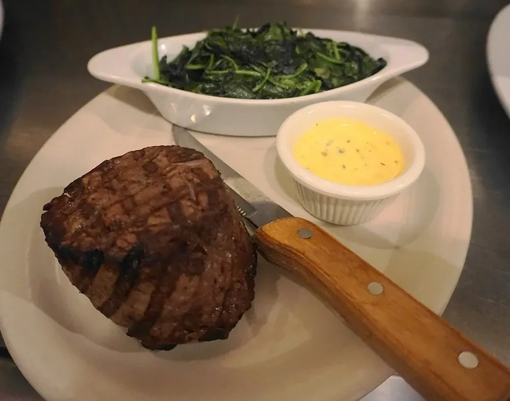Close-up overhead: grilled steak, creamy sauce, knife on white plate.