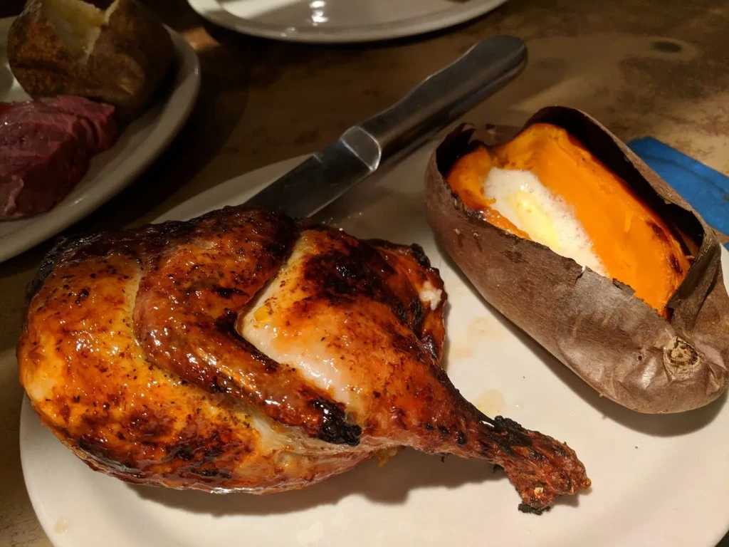 Close-up: Roasted chicken, split sweet potato with melted butter.