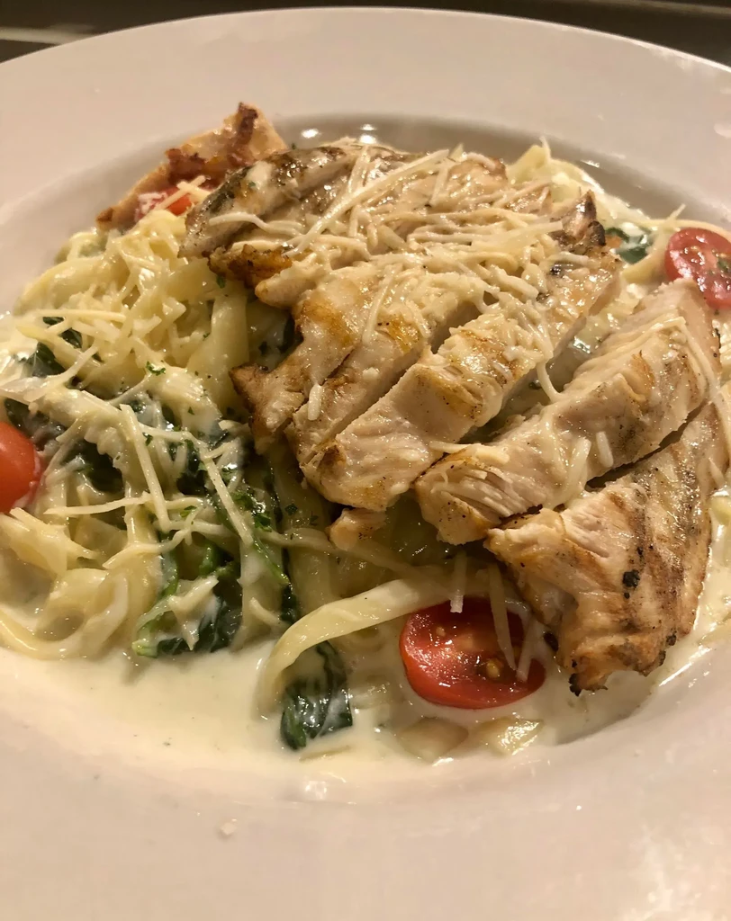 Creamy pasta with grilled chicken, cheese, spinach, and tomatoes.