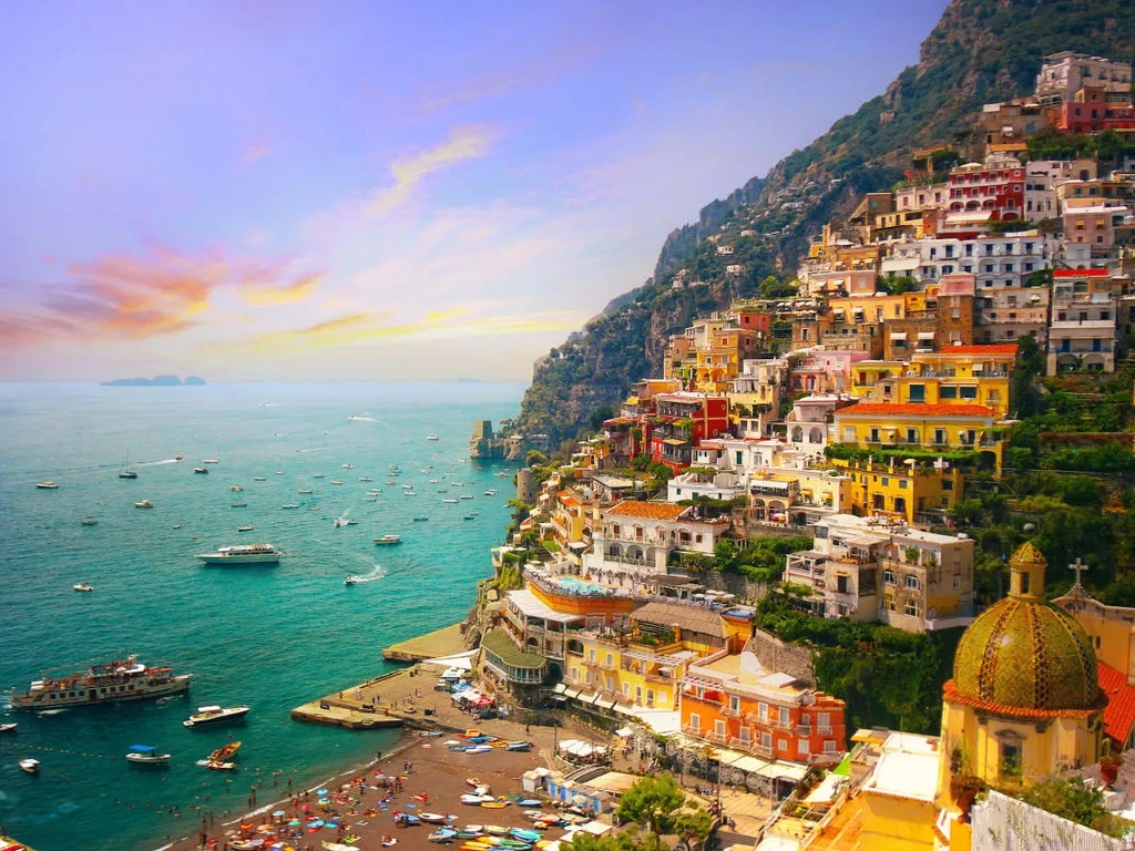 Colorful town cascading hillside to a turquoise sea with busy beach.