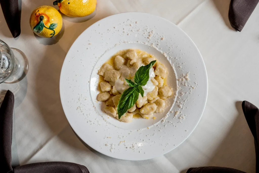 Overhead shot of gnocchi with creamy sauce, basil, and lemon shakers.