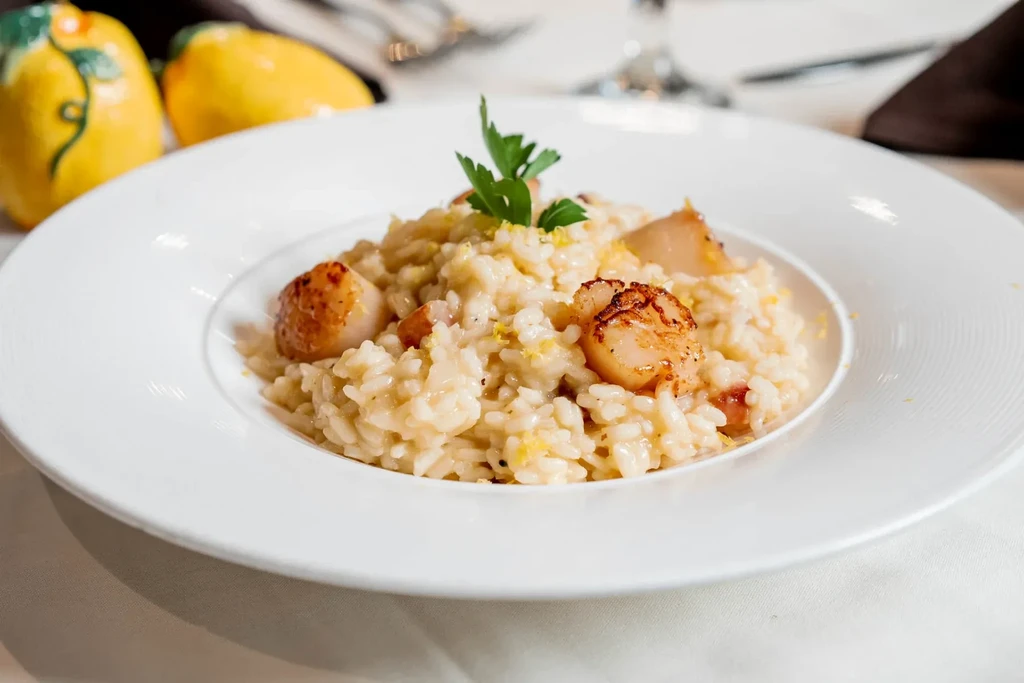 Creamy risotto with three golden-brown seared scallops, parsley and zest.