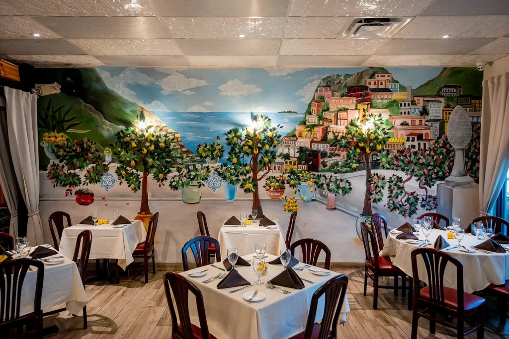 Empty restaurant dining room with Mediterranean mural and set tables.