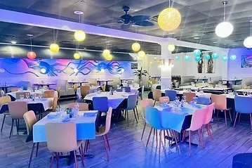 Modern restaurant interior with colorful lighting, abstract art, and pastel chairs.