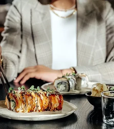 Close-up of sushi rolls with salmon, almonds, microgreens; chopsticks pick one.
