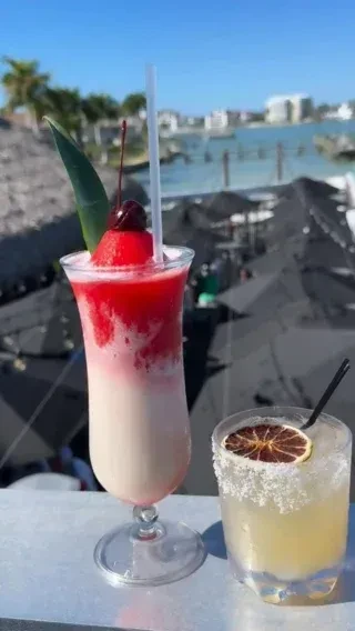 Two colorful cocktails on a reflective bar overlooking a sunny resort beach.